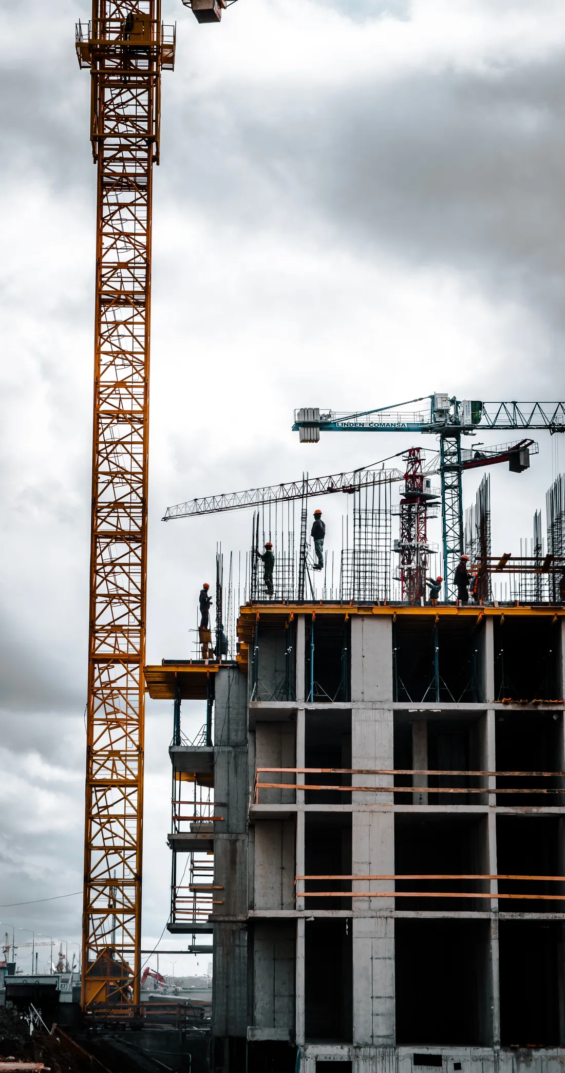 Gru a torre e operai al lavoro sull’ultimo solaio di un edificio in cemento armato